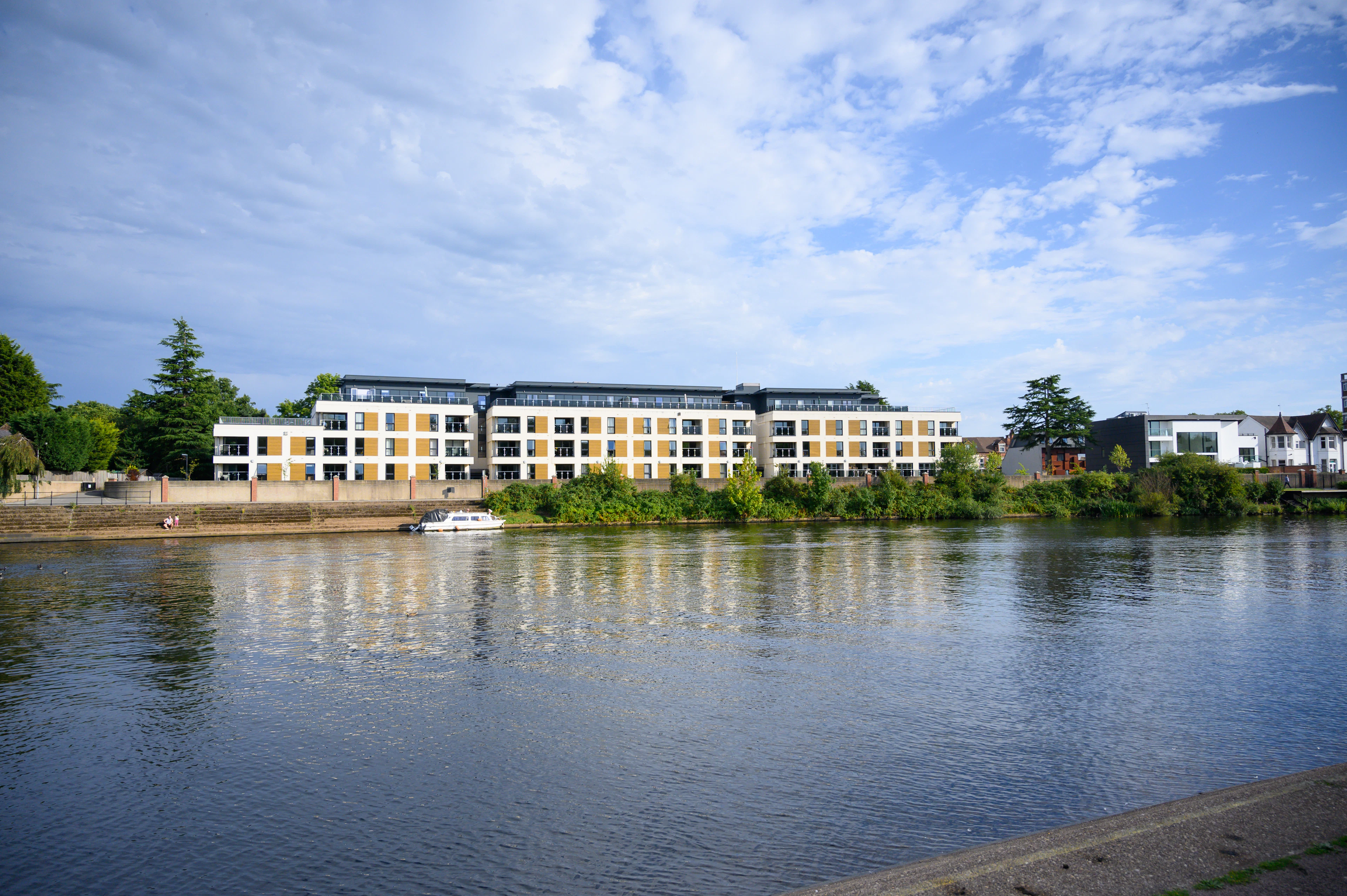 White low-rise apartments beside a lake under a blue sky
