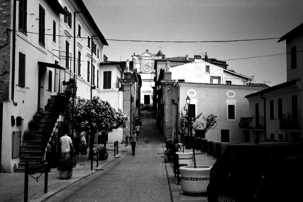 grayscale photo of people walking on sidewalk near buildings