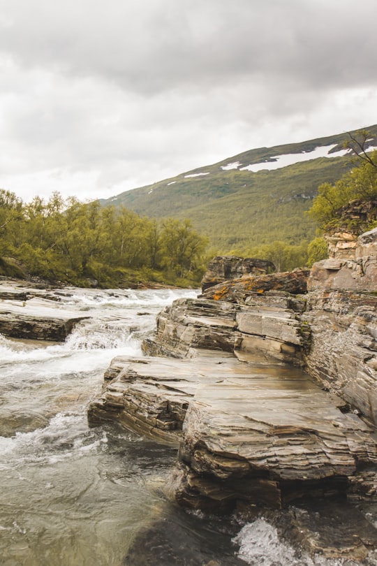brown rock formation on river during daytime in Abisko Sweden