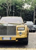 A luxurious Rolls Royce with gold accents showcased in a minimalist urban garage.