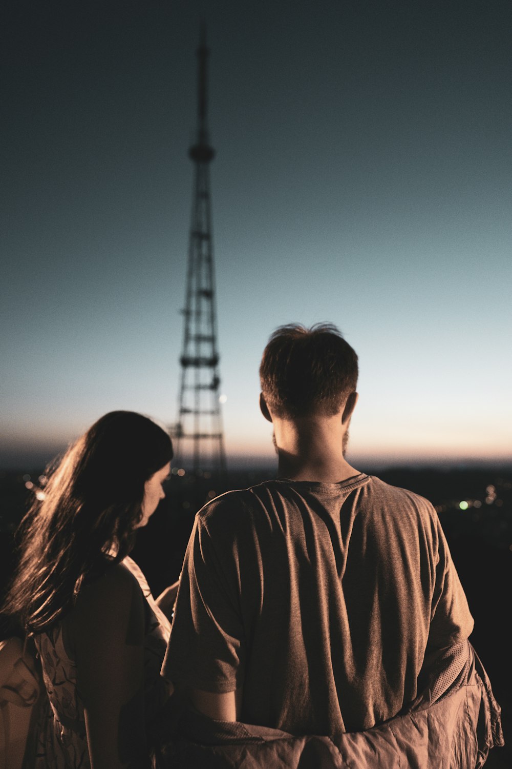 Silueta del hombre y de la mujer de pie cerca de la torre durante la puesta del sol