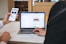 Two individuals are engaged in a collaborative setting. One person is holding a smartphone displaying a website, and the other is seated at a table with a laptop open, showing a job preference page. They seem to be reviewing or comparing information on both devices.