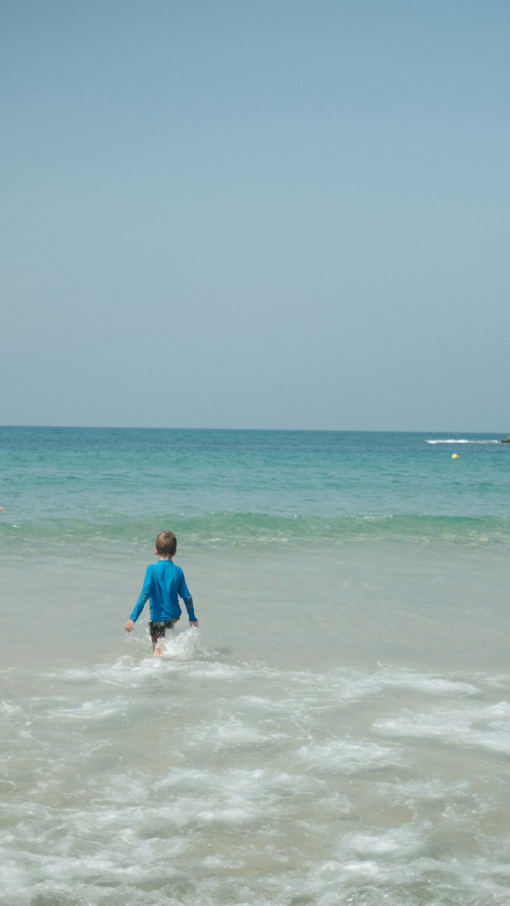 昼間、海でサーフィンをする青いシャツを着た男