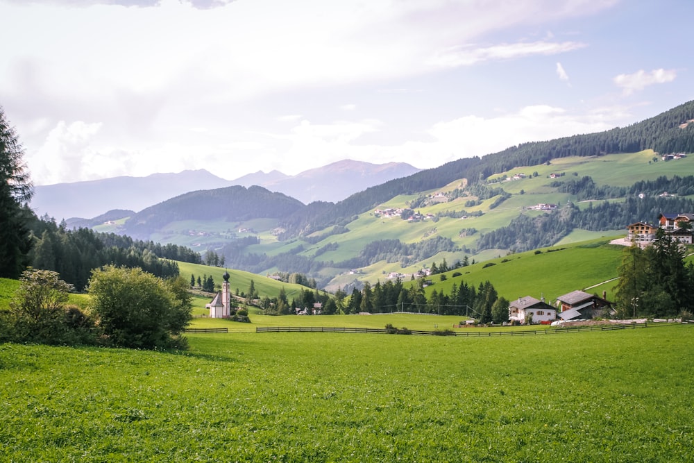 green grass field near green mountains under white clouds during daytime