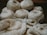 Several skeins of cream-colored yarn sit in the background, while knitting needles hold a partly-knitted fabric in the foreground. The scene suggests a cozy, crafty atmosphere.
