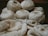 Several skeins of cream-colored yarn sit in the background, while knitting needles hold a partly-knitted fabric in the foreground. The scene suggests a cozy, crafty atmosphere.