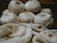 Several skeins of cream-colored yarn sit in the background, while knitting needles hold a partly-knitted fabric in the foreground. The scene suggests a cozy, crafty atmosphere.