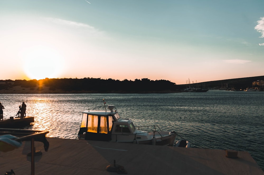 people sitting on brown wooden bench near body of water during sunset