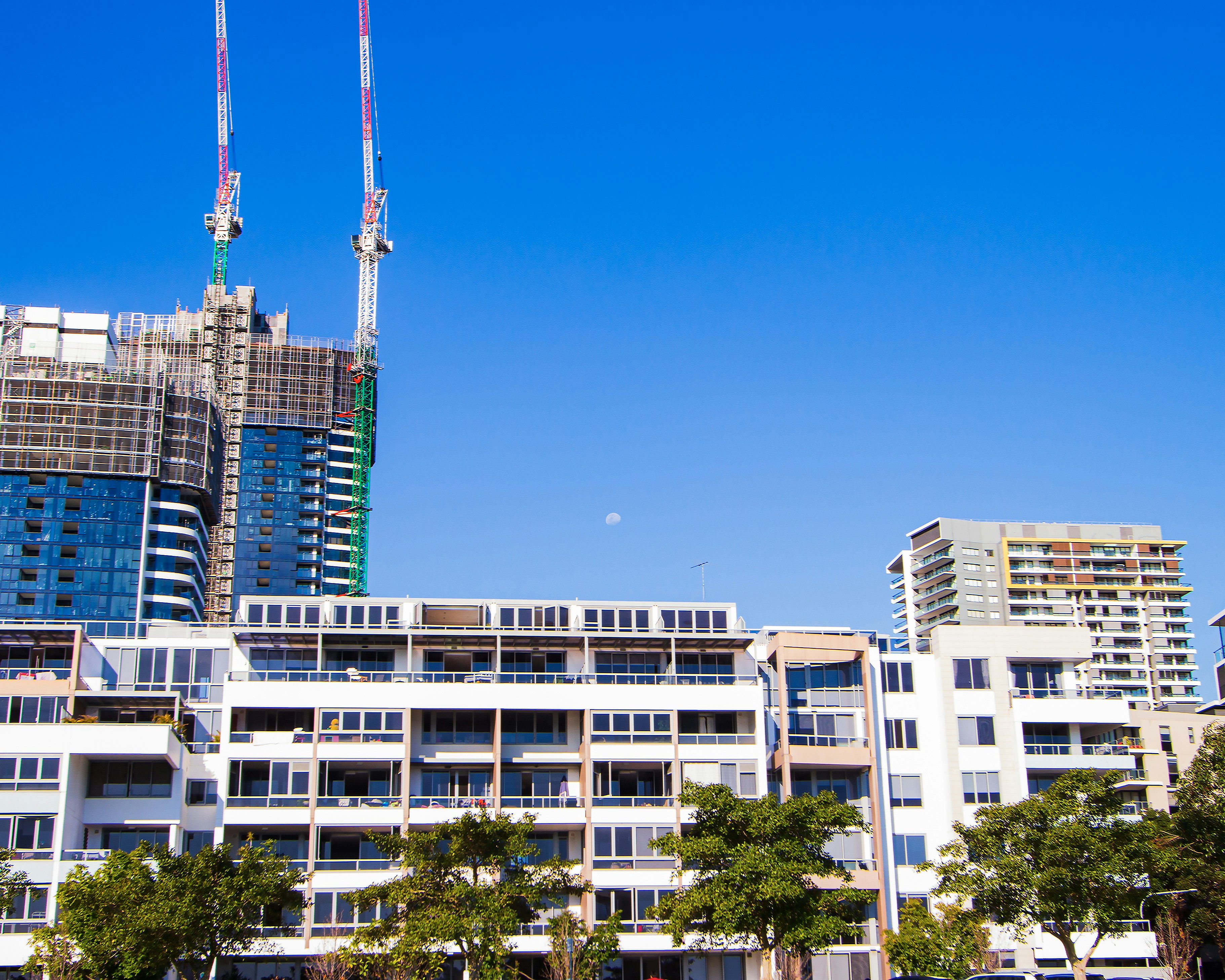 Modern apartment building under construction with concrete structure, scaffolding and cranes against blue sky, active development site