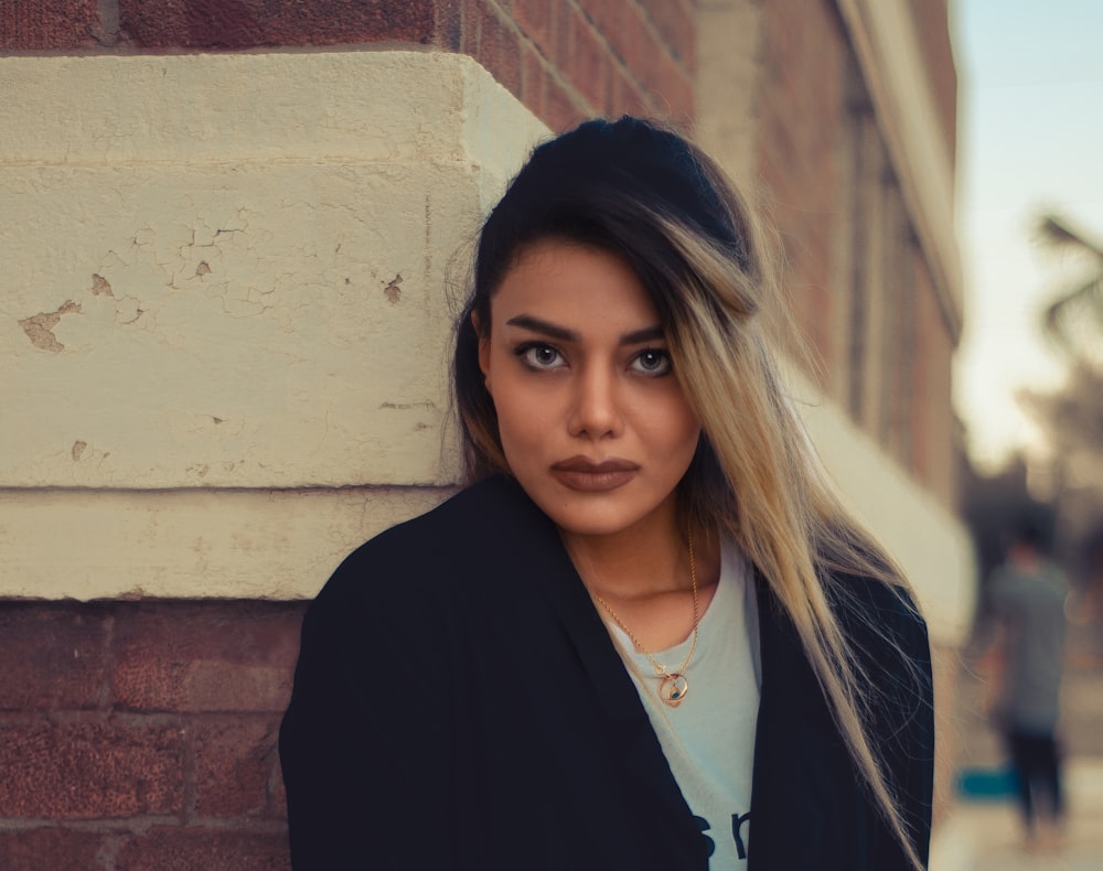 woman in black cardigan standing beside brown brick wall