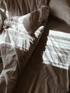Natural light casting soft shadows on folded bed linens made from sustainable fibers.