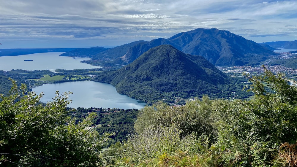 green trees on mountain near lake under white clouds and blue sky during daytime