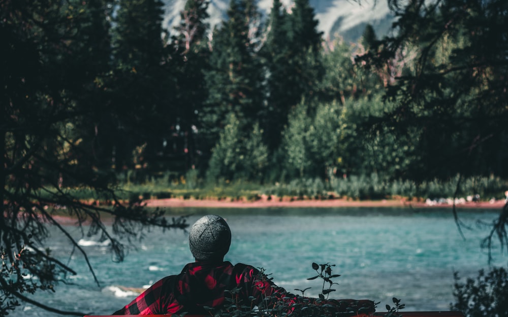 person in red and black jacket sitting on black bench near body of water during daytime