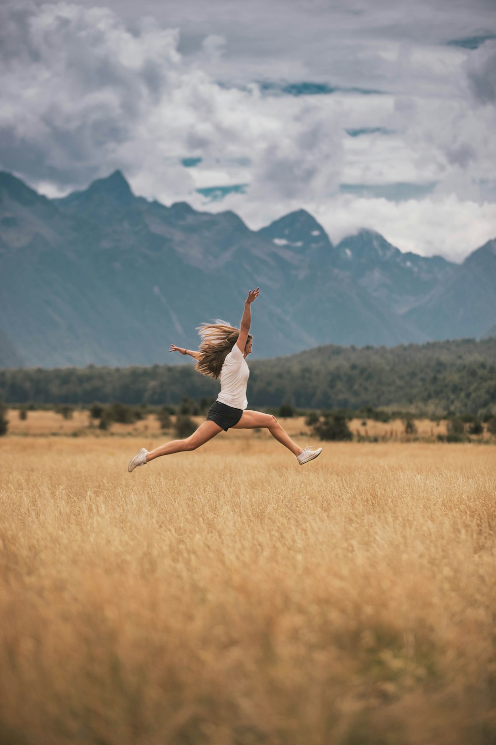 woman in black tank top and white shorts jumping on brown grass field during daytime