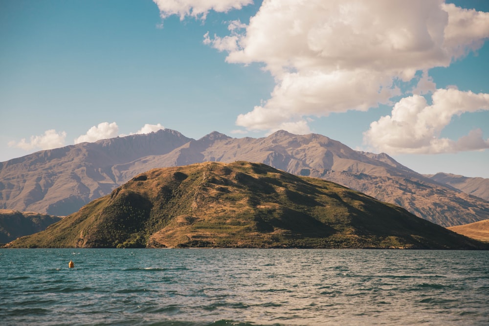 brown and green mountain beside body of water under blue sky and white clouds during daytime