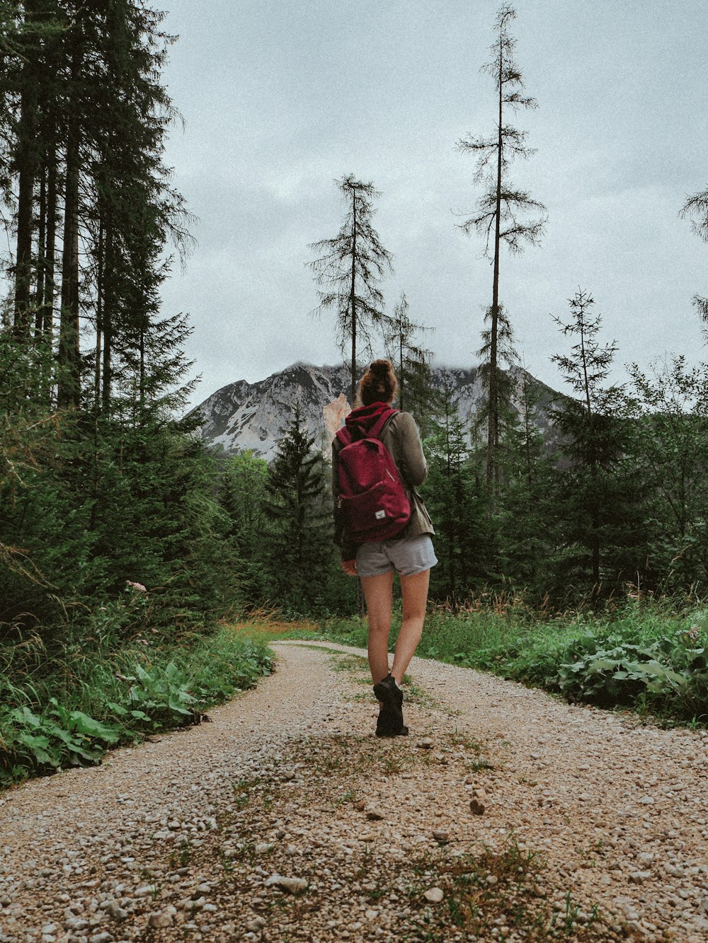 woman in red jacket standing on dirt road between trees during daytime