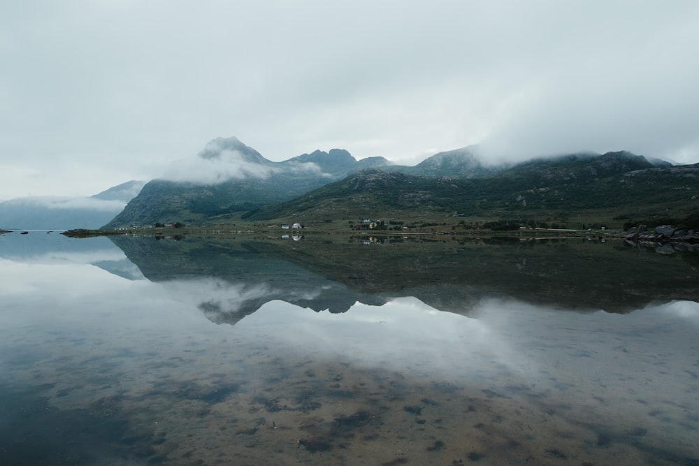 green mountain beside body of water under white clouds during daytime