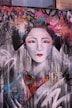 A large mural featuring a stylized portrait of a woman with traditional Japanese makeup and attire. The background is filled with vibrant graffiti and abstract patterns, including doodles and spray-painted flowers in various colors.