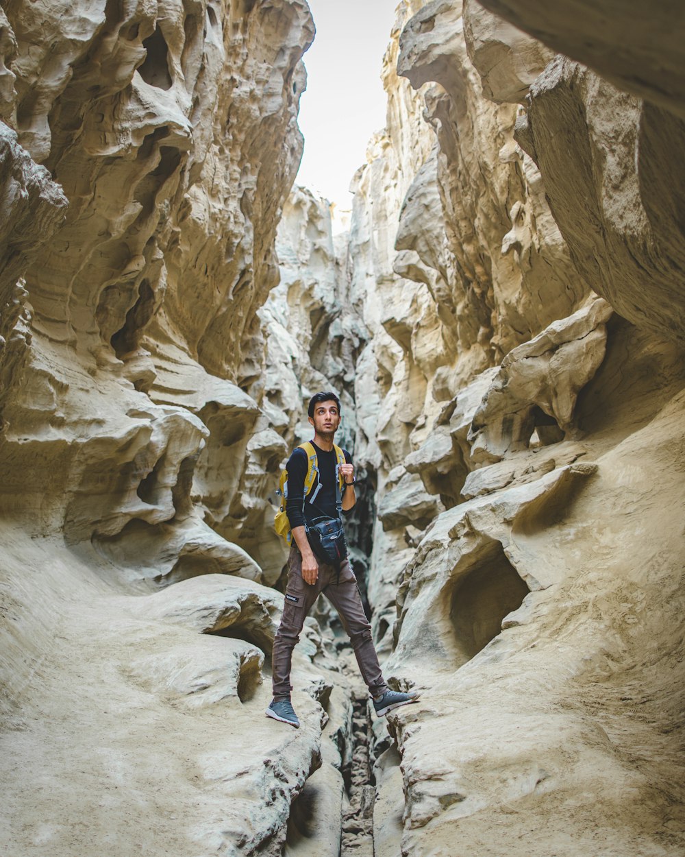 man in black and red jacket and blue denim jeans standing on rocky mountain during daytime