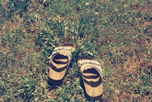 A pair of bamboo sandals worn on a sunlit wooden deck surrounded by green plants.
