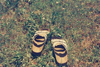 A pair of sandals displayed outdoors on a sunlit stone path surrounded by greenery.