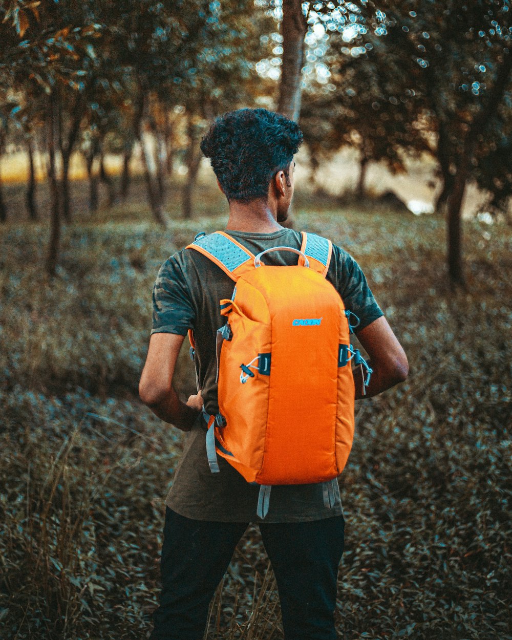 man in orange and black backpack standing on brown dried leaves during daytime