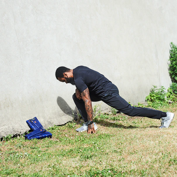 An athlete stretching in a black and orange Nuifit tracksuit against an urban graffiti wall.