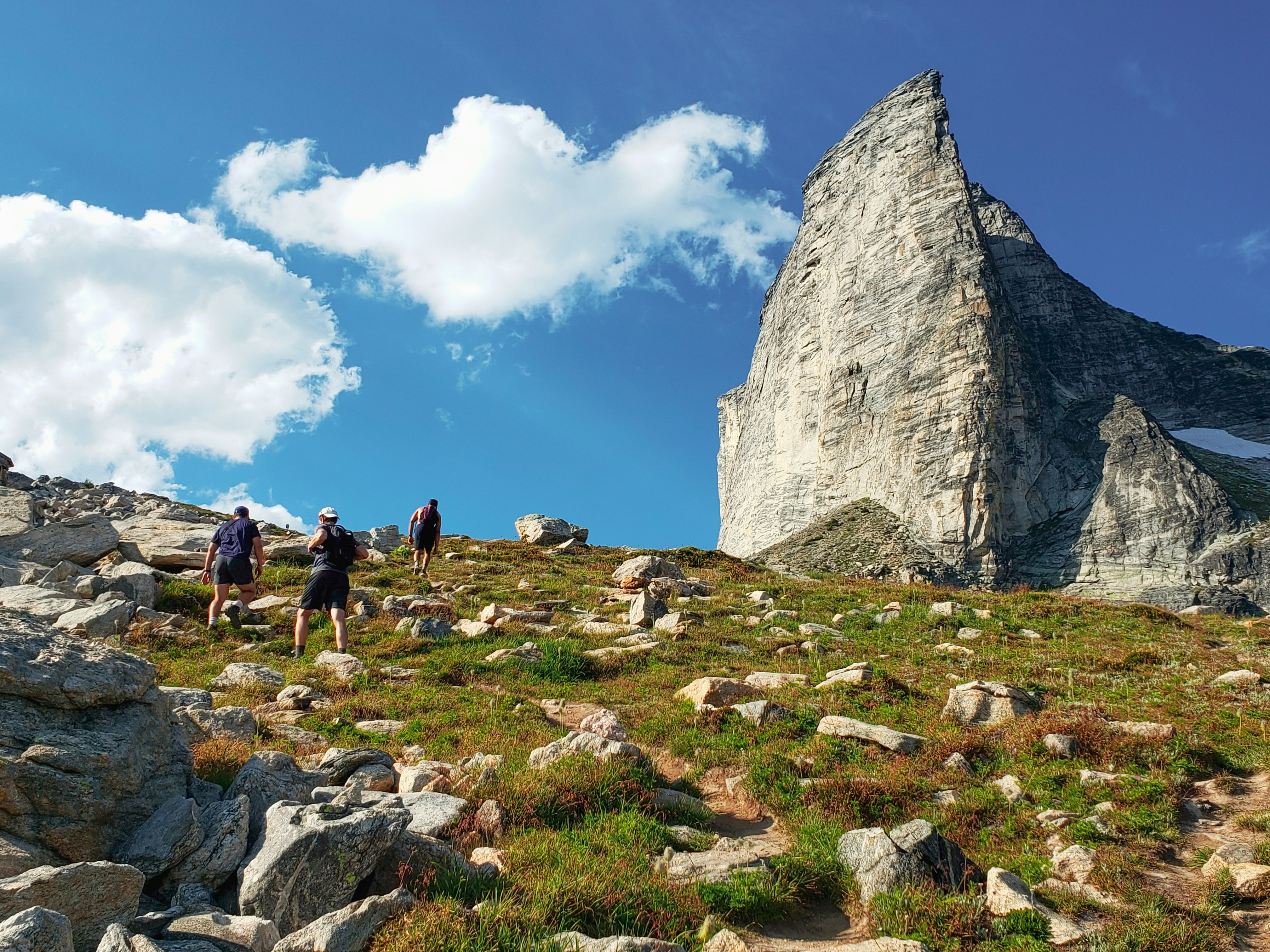 people walking on green grass field near gray rock formation under blue and white sunny cloudy