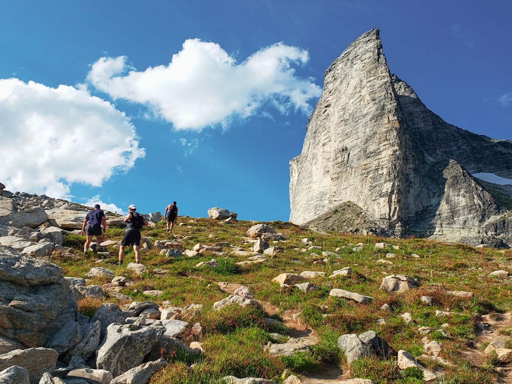 people walking on green grass field near gray rock formation under blue and white sunny cloudy