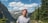 man in white crew neck t-shirt standing near green trees and mountains during daytime