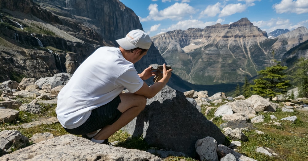 man in white t-shirt and black shorts sitting on rock mountain during daytime