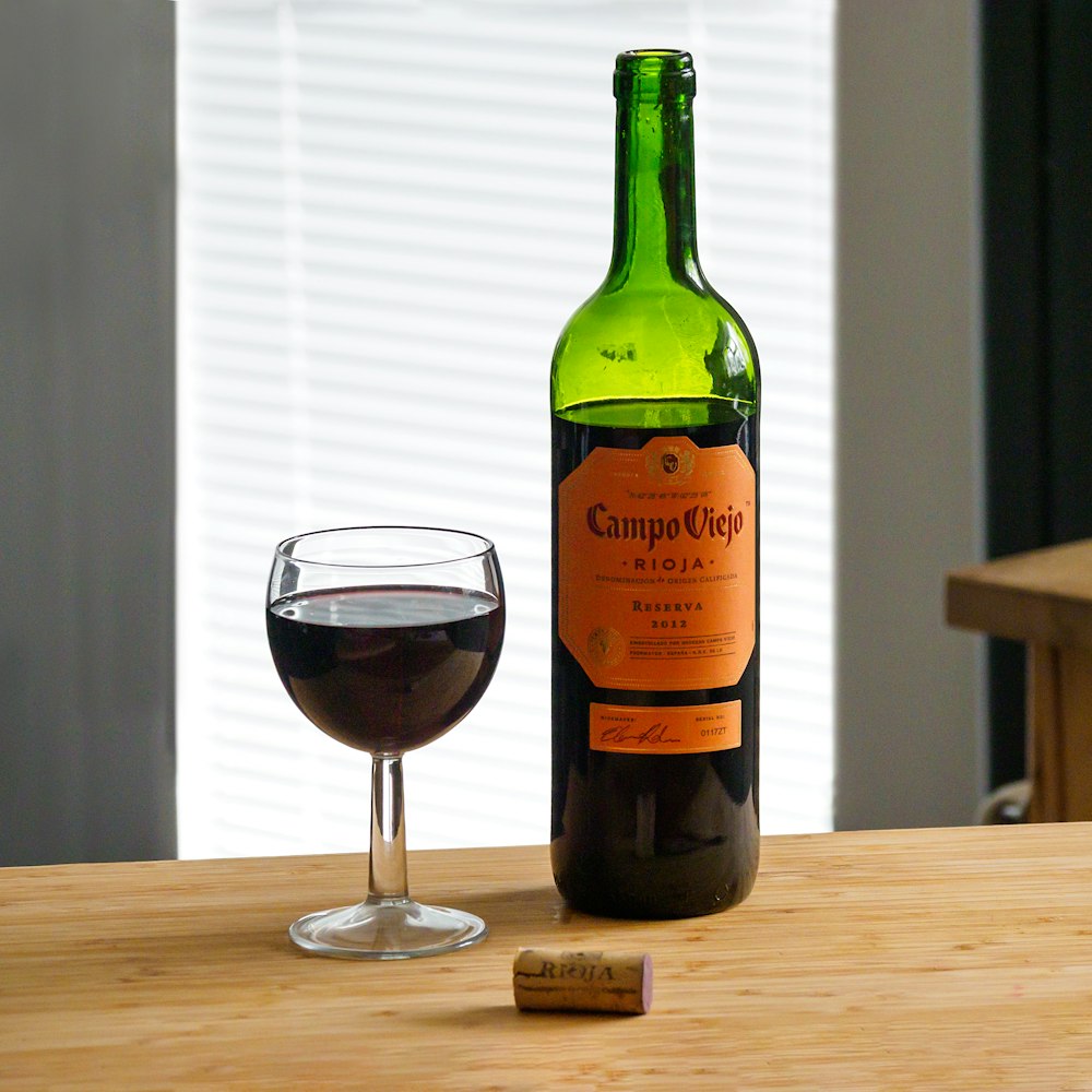 green glass bottle beside clear wine glass on brown wooden table