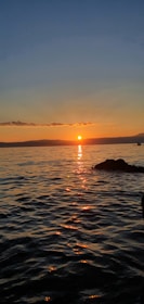 A golden sunset casting warm light over the calm sea and a sleek yacht silhouette.