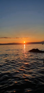 A golden sunset casting warm light over the calm sea and a sleek yacht silhouette.