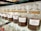 A row of glass jars filled with different types of coffee beans, each labeled with a specific blend, such as Viennese Blend, Oriental Espresso Blend, and Arabica Plantation-AAA. The jars are neatly aligned on a glass shelf, and the coffee beans inside are varying shades of brown.