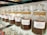 A row of glass jars filled with different types of coffee beans, each labeled with a specific blend, such as Viennese Blend, Oriental Espresso Blend, and Arabica Plantation-AAA. The jars are neatly aligned on a glass shelf, and the coffee beans inside are varying shades of brown.