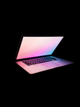 A sleek, modern laptop with glowing gradient lights reflecting the colors #9747ff, #00fff2, and #00ffae on a clean desk setup.