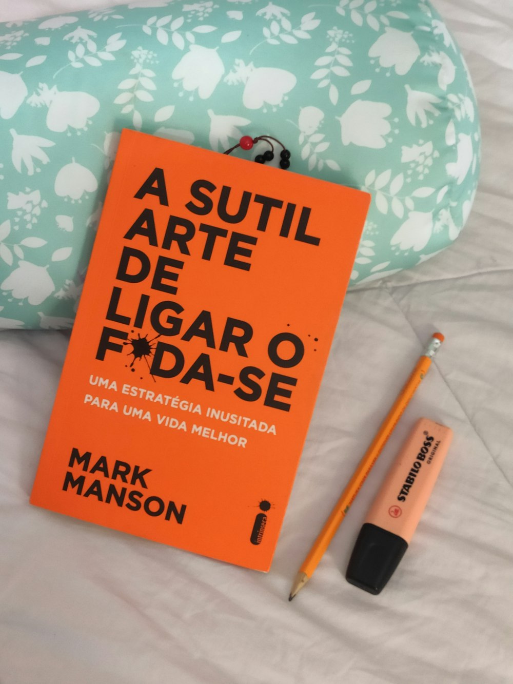 Ein orangefarbenes Buch sitzt auf einem Bett neben einem Stift