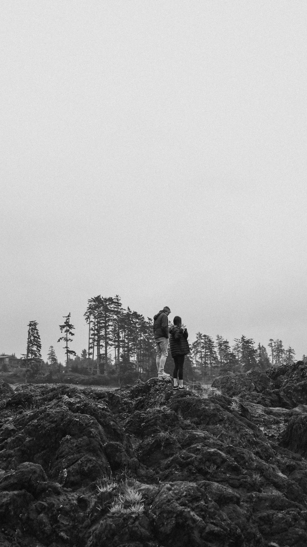 grayscale photo of 2 men standing on rock