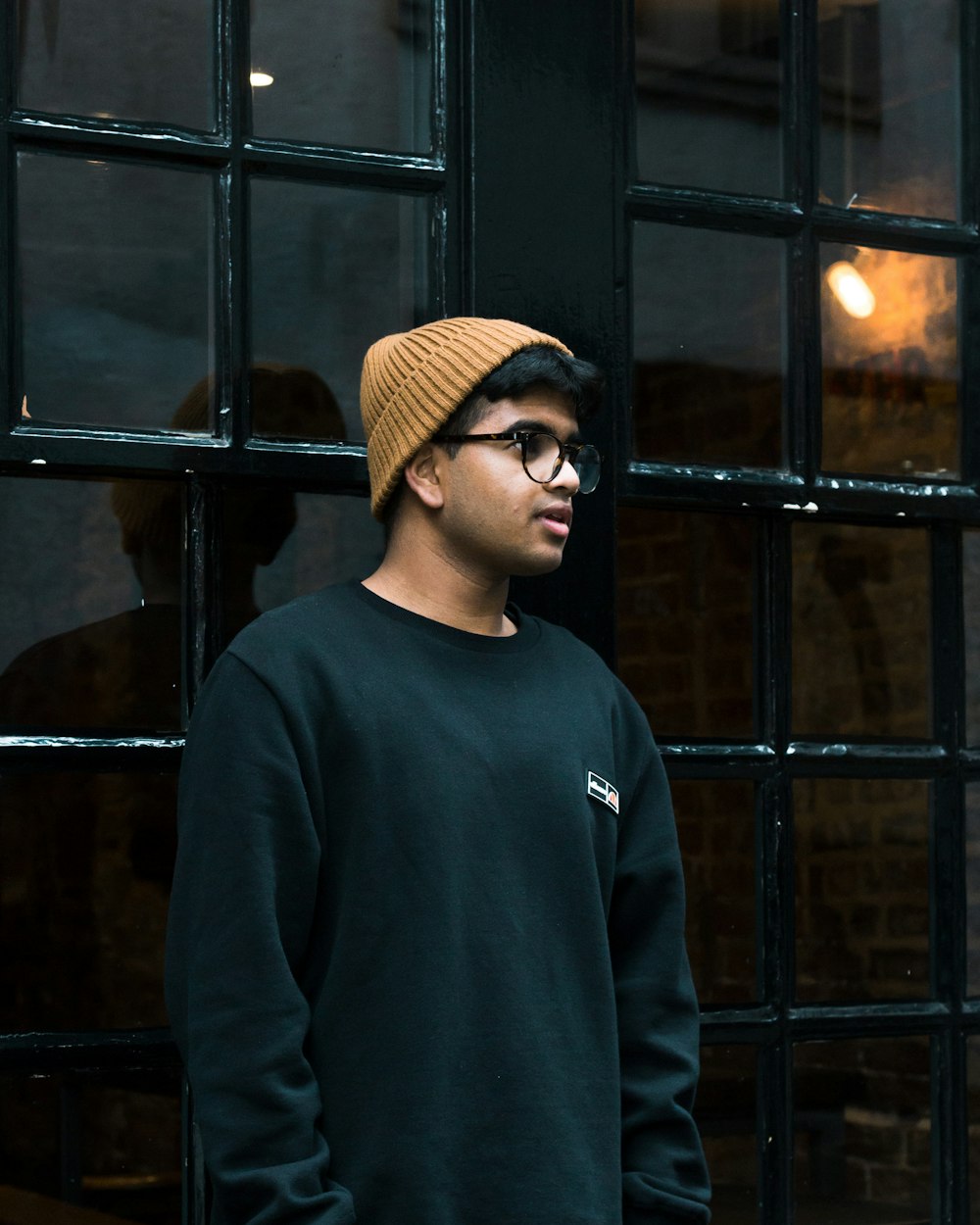 man in black sweater wearing brown knit cap and black framed eyeglasses