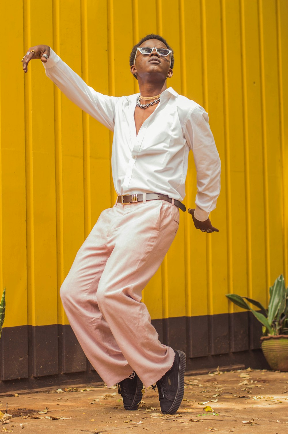 homem na camisa social branca e calças beges de pé ao lado da parede amarela