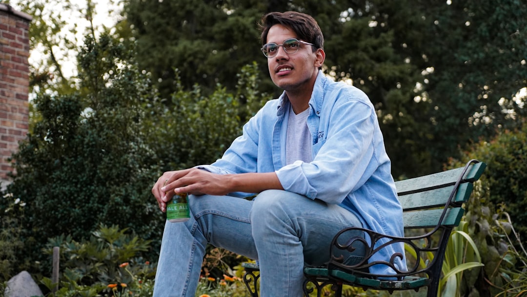 man in blue dress shirt and blue denim jeans sitting on black metal bench during daytime