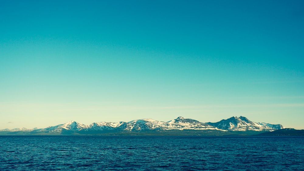 mar azul perto da montanha coberta de neve sob o céu azul durante o dia