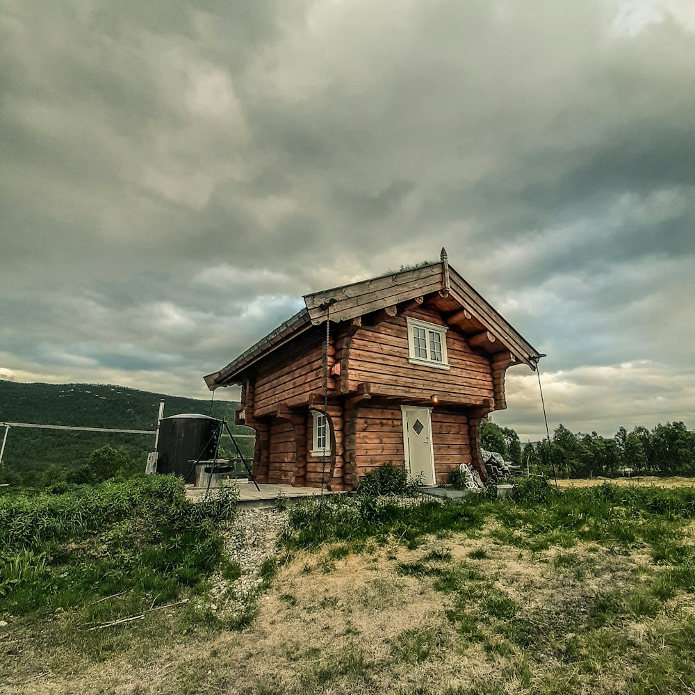maison en bois marron sur un champ d’herbe verte sous un ciel nuageux gris pendant la journée