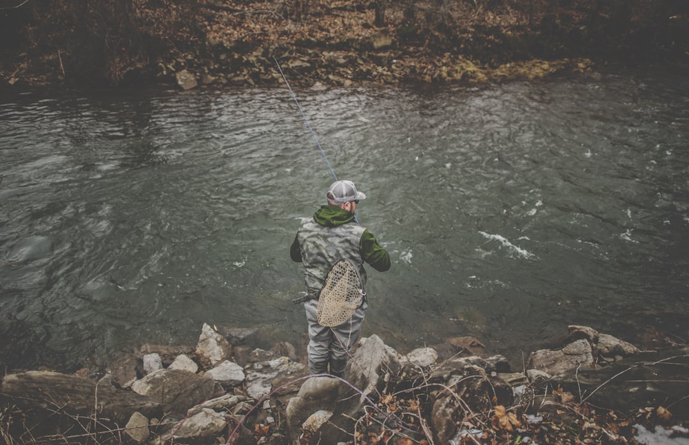 man in gray jacket and black pants fishing on river during daytime