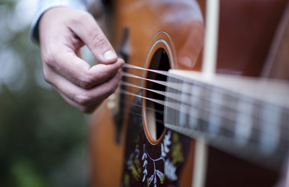 Persona tocando la guitarra acústica marrón