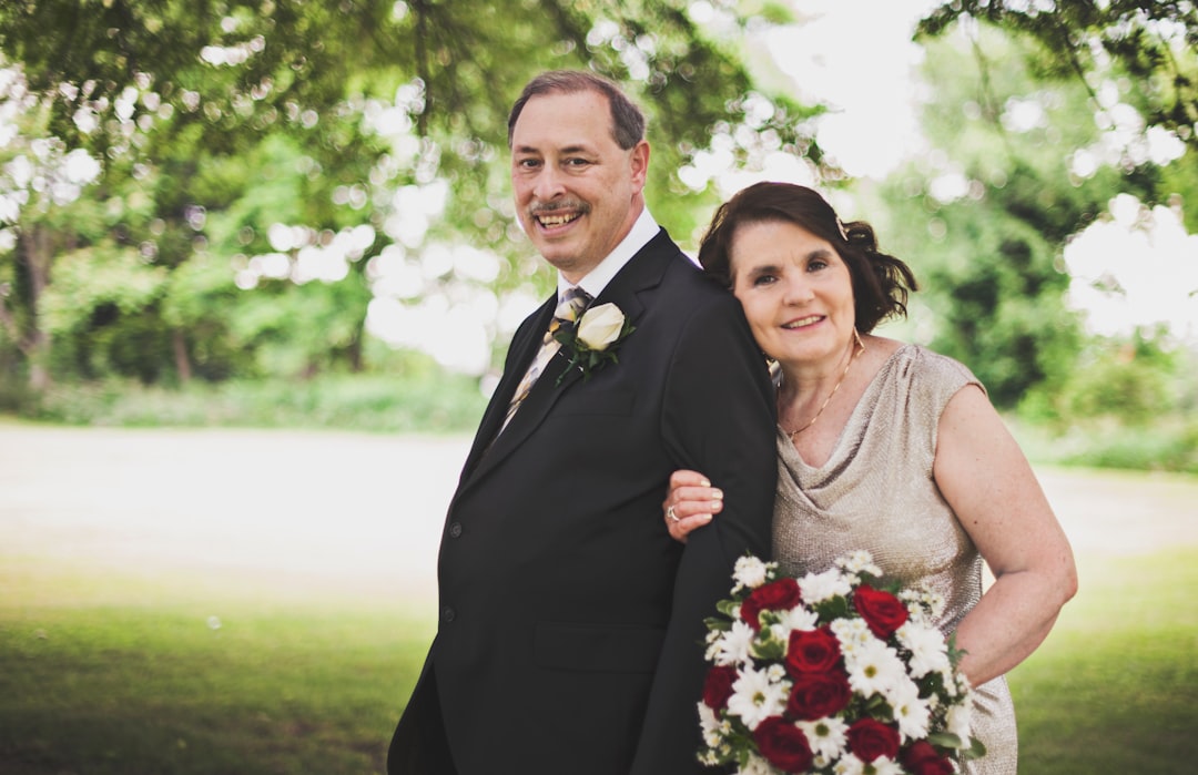 man in black suit standing beside woman in gray sleeveless dress holding bouquet of flowers