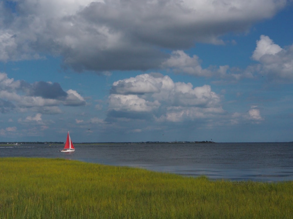 white and red sailboat on sea under white clouds and blue sky during daytime