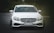 A sleek white Mercedes-Benz car is parked on a dark road with greenery in the background. The car's front view is captured, showcasing its elegant grille and shiny headlights. The license plate reads '50LD-151.75'. The overall setting is dimly lit, highlighting the vehicle's features.