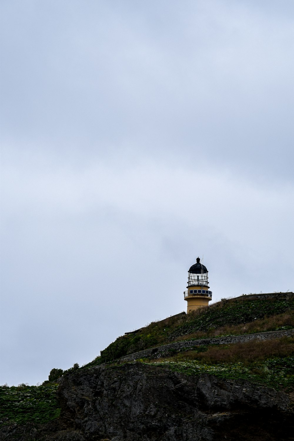 Weißer und schwarzer Leuchtturm auf grünem Gras bedecktem Hügel unter weißem, bewölktem Himmel während des Tages